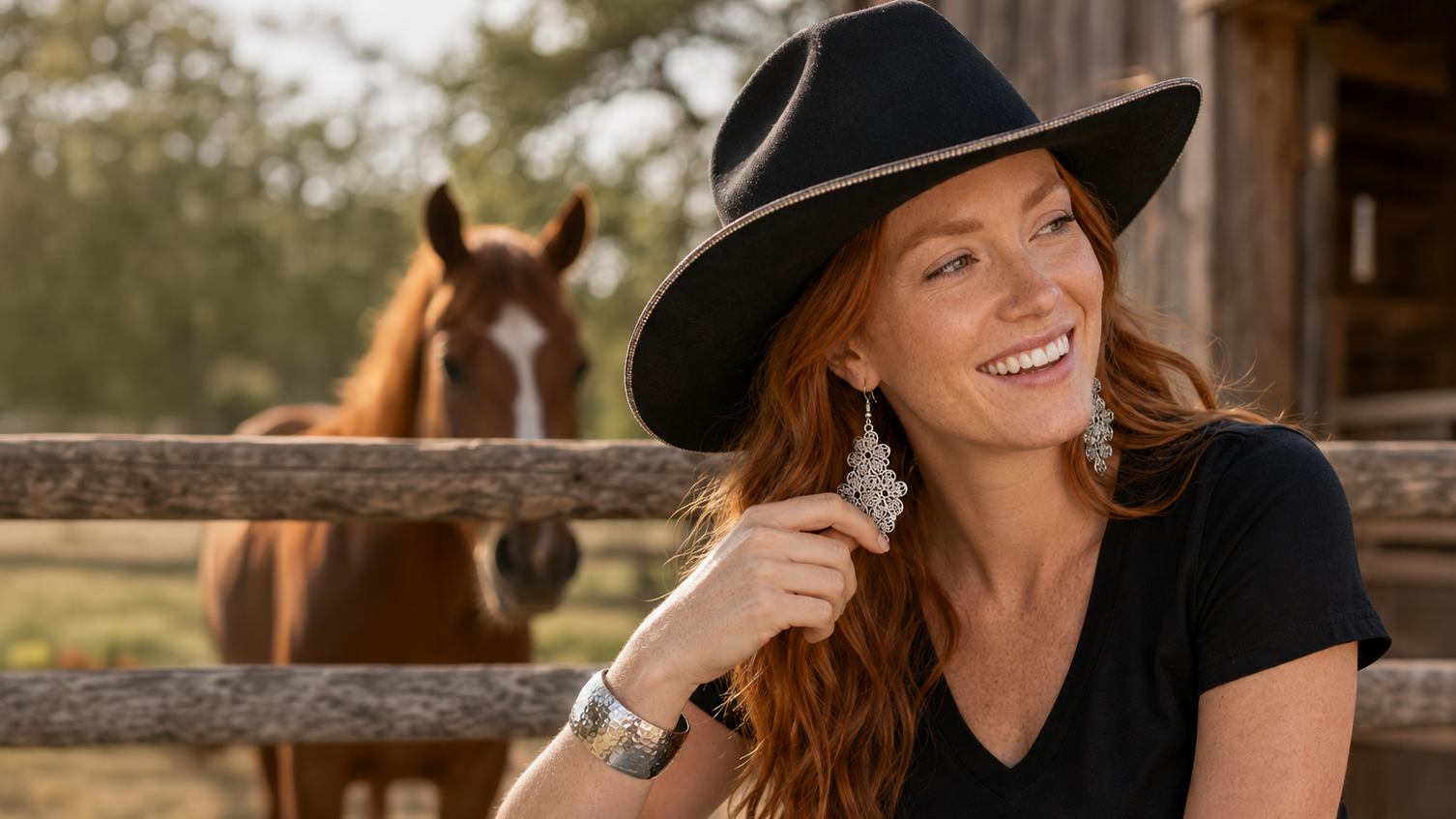 Silver floral drop earrings worn by a woman wearing a cowboy hat sitting in front of a fence