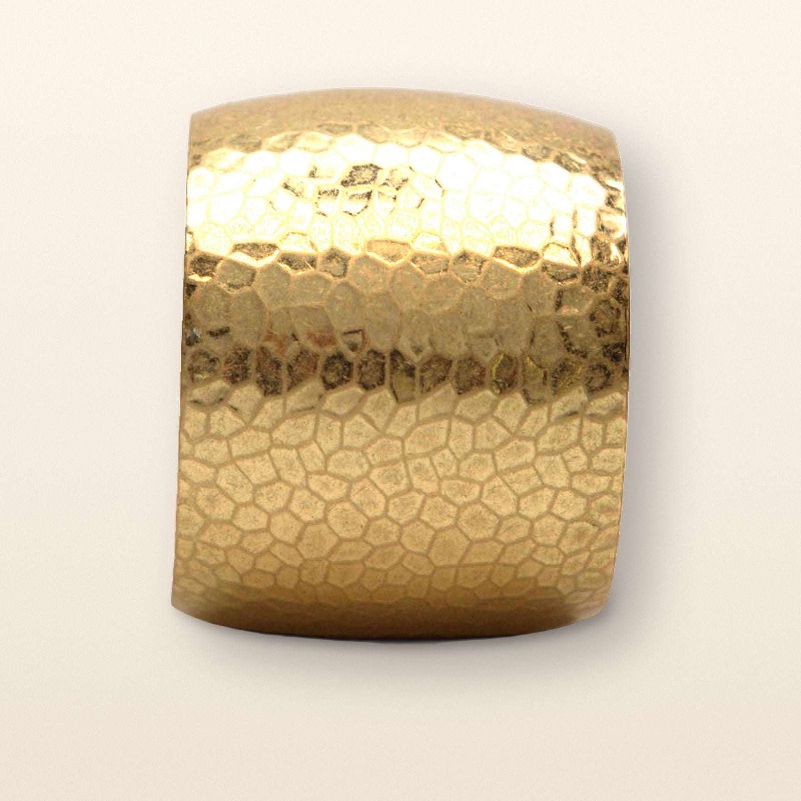 Hammered gold cuff bracelet shown close-up against a warm neutral background.